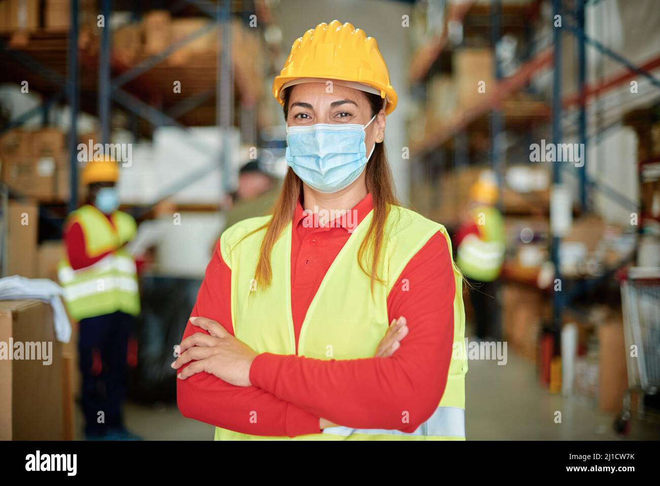 Ritratto di una donna felice che guarda la telecamera all'interno del magazzino Durante l'uso della maschera facciale - mettere a fuoco sul viso Foto Stock