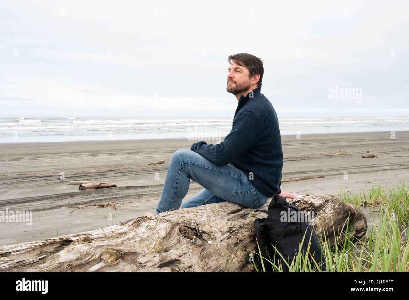 Uomo seduto e godendo nuvoloso Pacific Northwest spiaggia Foto Stock