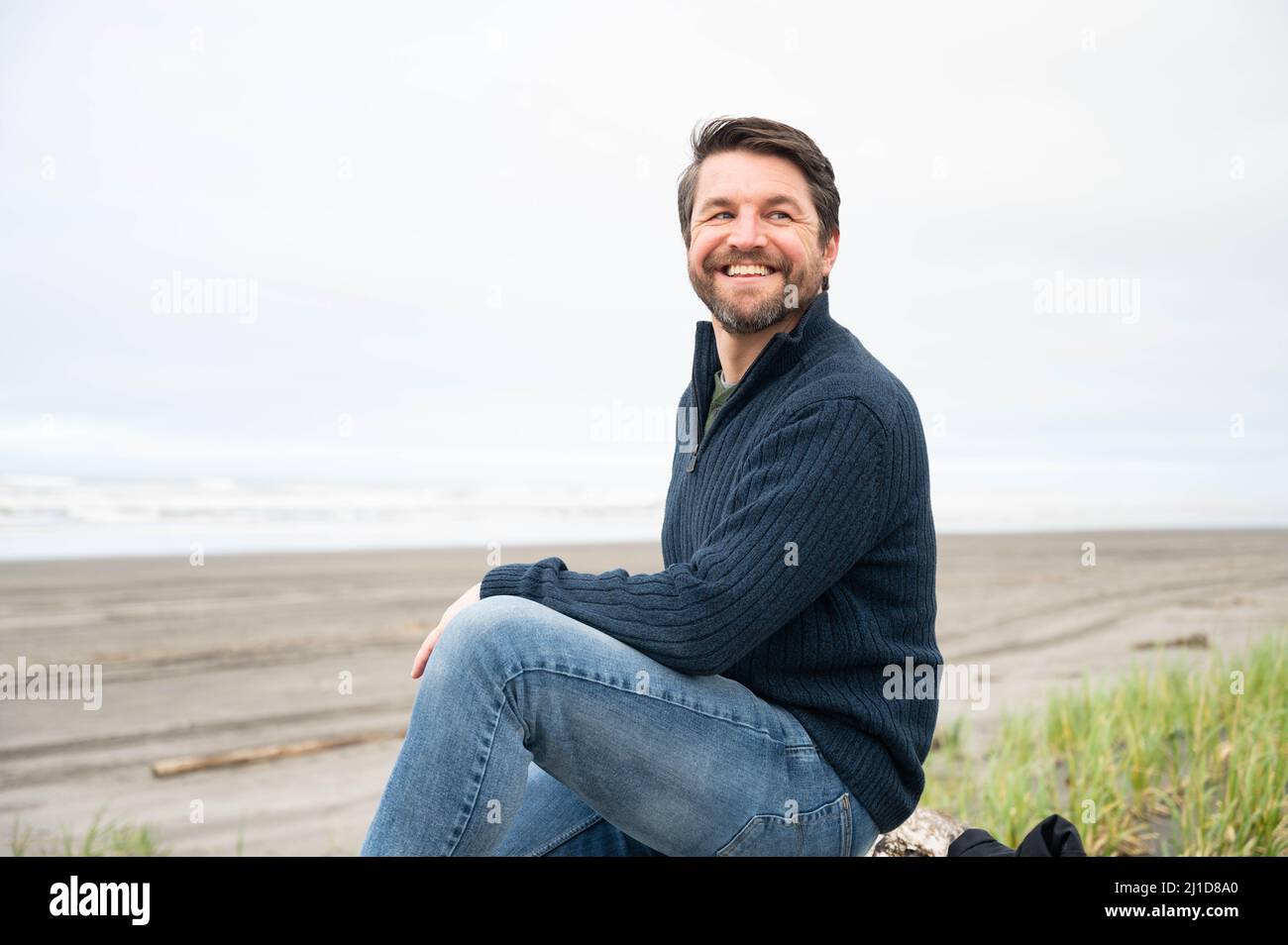 Uomo seduto e godendo nuvoloso Pacific Northwest spiaggia Foto Stock