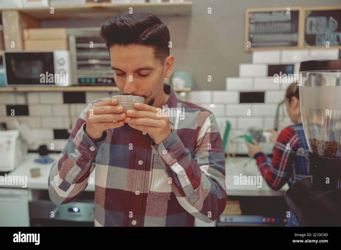 Giovane barista in camicia a quadri degustazione caffè Foto Stock