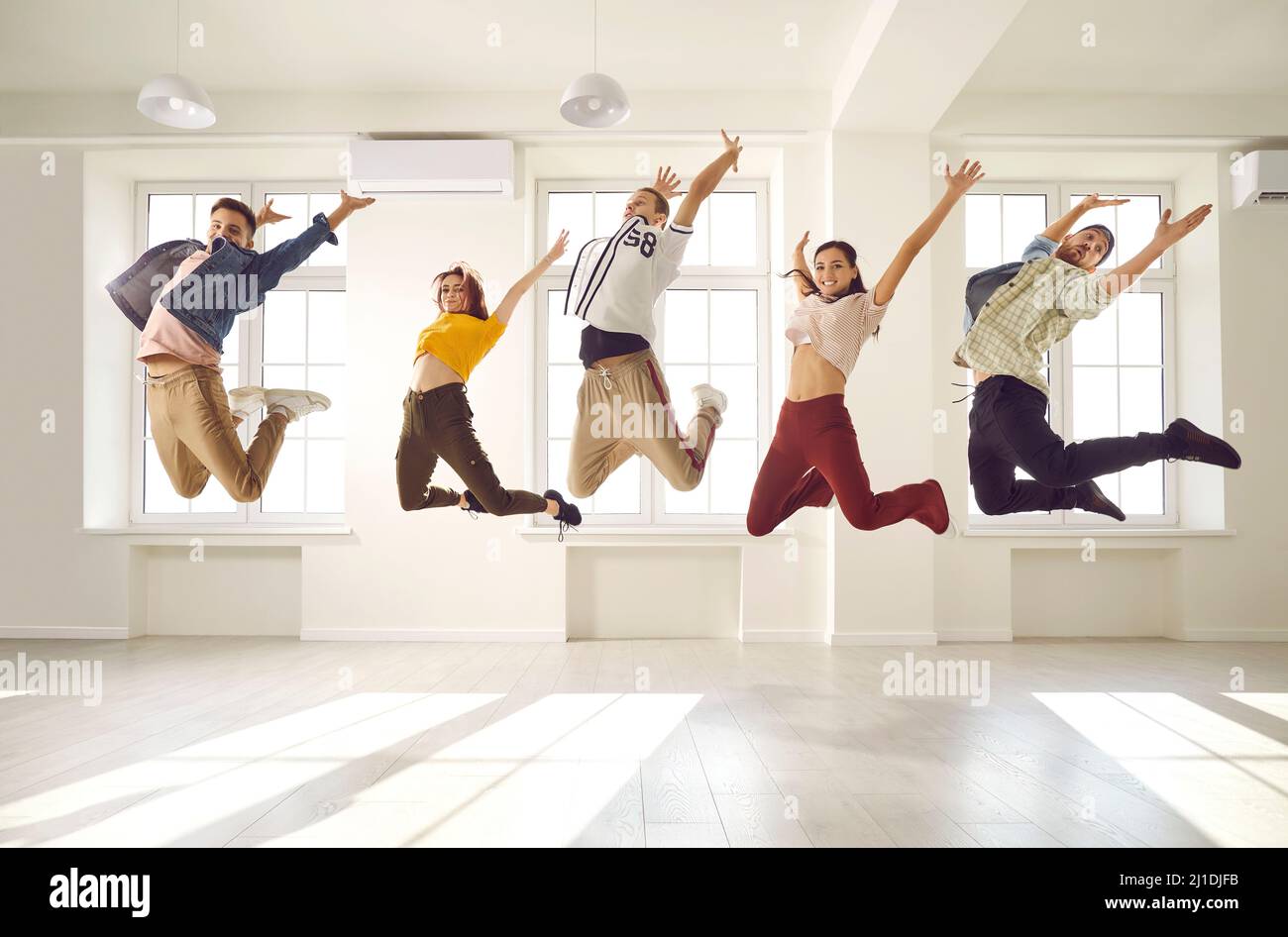 Gruppo di ballerini felici e contemporanei che si divertono e saltano in alto nell'aria insieme Foto Stock