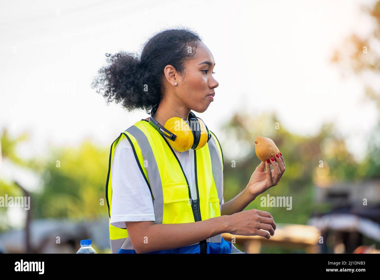 Smile African american donna uomo di lavoro o ingegnere di manutenzione donna in riflettente giubbotto di sicurezza siede giù su vecchio camion per rilassarsi, mangia Foto Stock