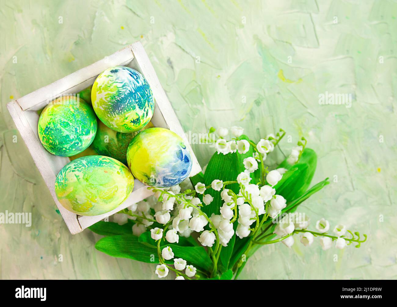 Uova colorate in scatola con gigli della valle su sfondo verde menta astratto. Pasqua. Spazio di copia Foto Stock
