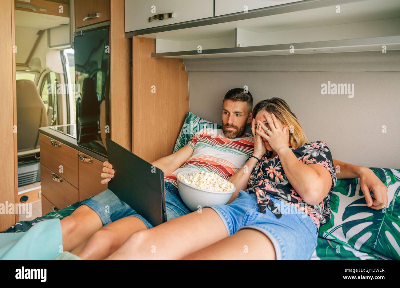 Giovane coppia che guarda un film spaventoso sulla tavoletta sdraiata sul letto del loro camper. Foto Stock