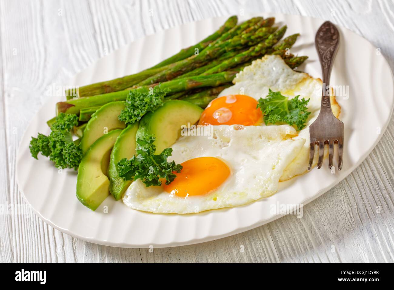 primo piano di asparagi arrostiti, avocado fresco maturo e uova fritte con tuorli runny su un piatto bianco Foto Stock