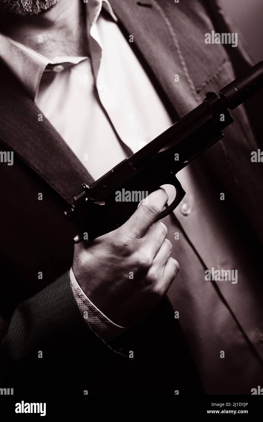 Ben vestito agente segreto maschile detective spia indossare vestito e cravatta tenuta pistola automatica. Foto Stock