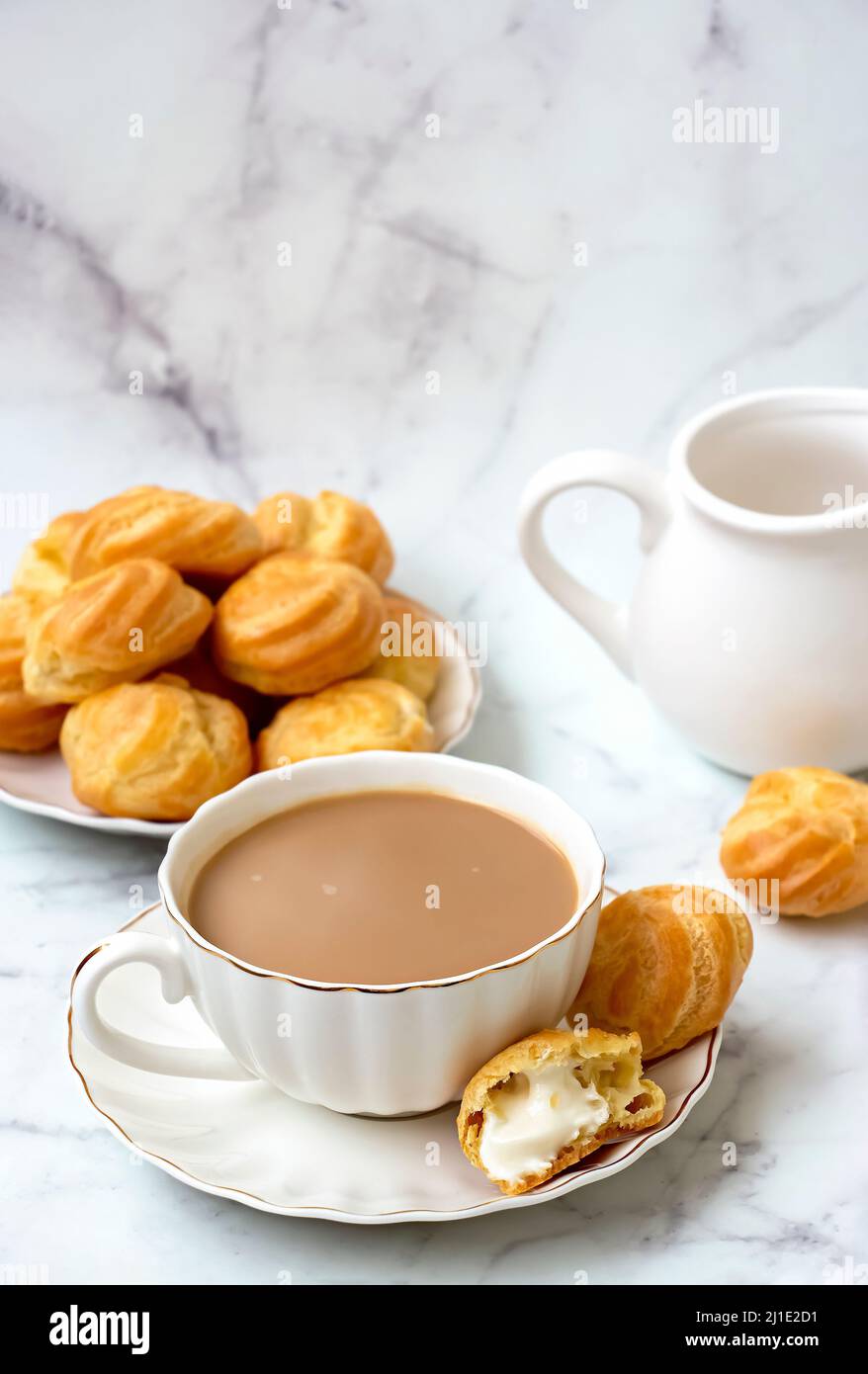 Karak chai o Masala tè e profiteroles fatti in casa farciti con panna montata. Su sfondo chiaro di marmo. Foto Stock