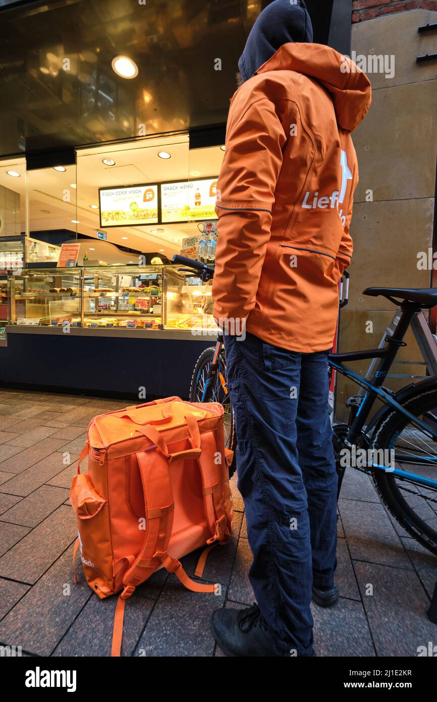 20.12.2021, Germania, Brema, Brema - giovane corriere dal servizio di consegna alimentare Lieferando attende l'ordine per il cliente al fast food re Foto Stock