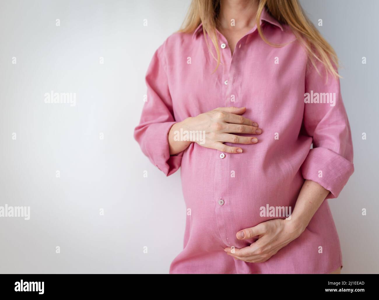 una donna incinta in una camicia rosa si erge su uno sfondo bianco Foto Stock