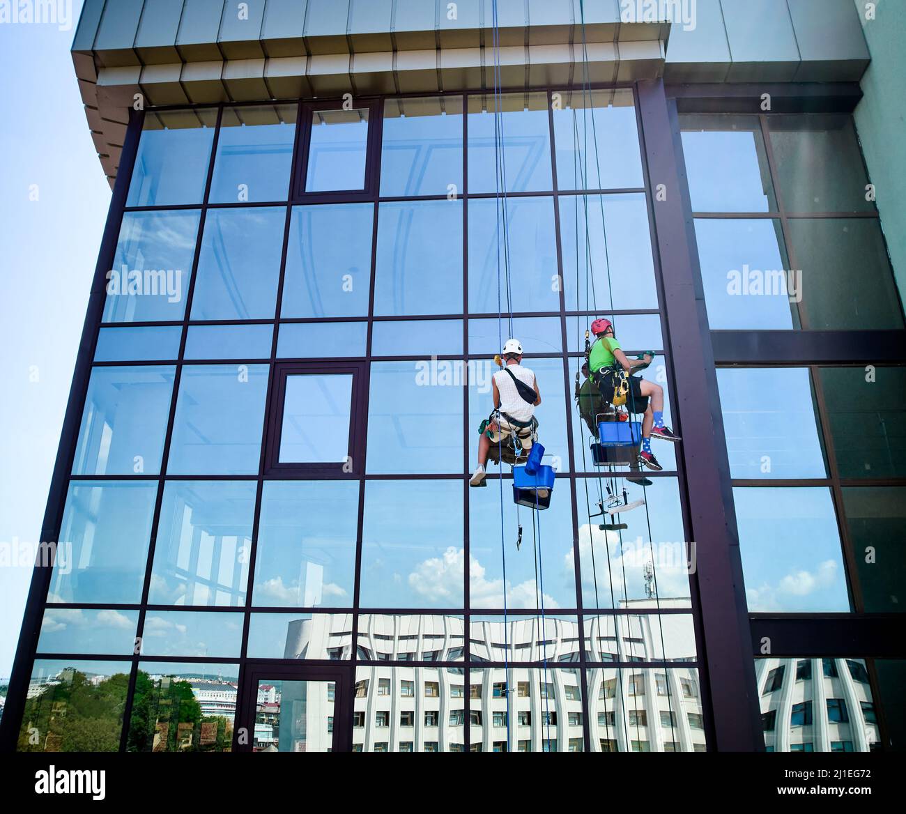 Lavoratori di alpinismo industriale lavano finestre in vetro di un alto edificio, appesi su funi di arrampicata di sicurezza. Due pulitori per finestre uomini che lavorano insieme all'esterno del grattacielo. Foto Stock