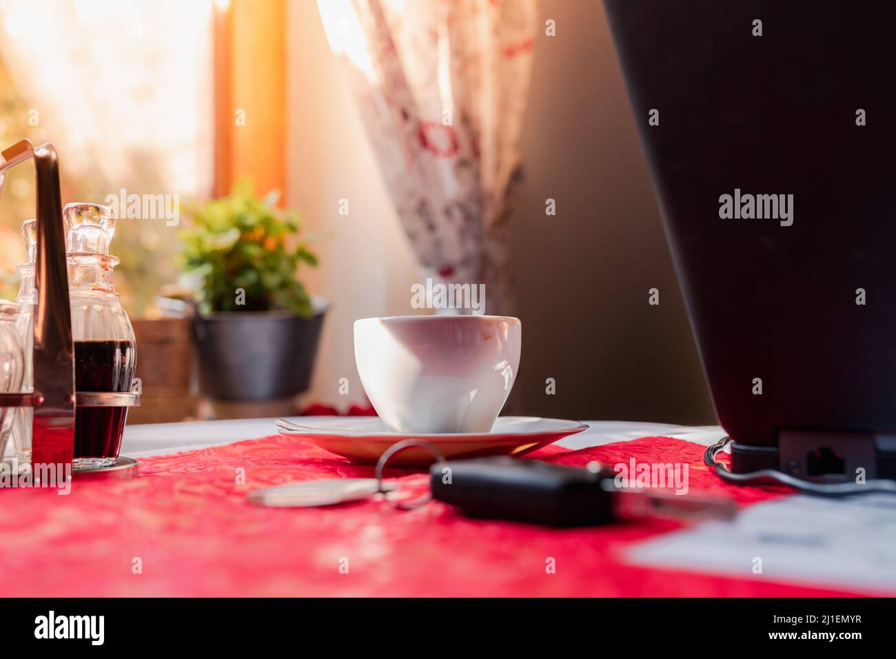 tazza di caffè, chiavi dell'auto e computer portatile sul tavolo del caffè al sole. Lavoro freelance online Foto Stock