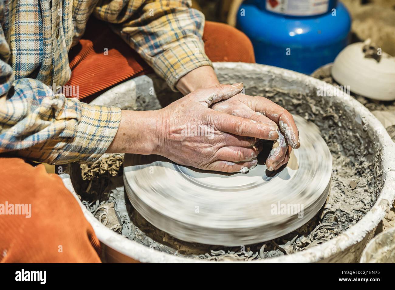 Mani muscolari di uomo di mezza età, vasaio, sporcato in argilla, forma ceramica da argilla sulla ruota del vasaio Foto Stock