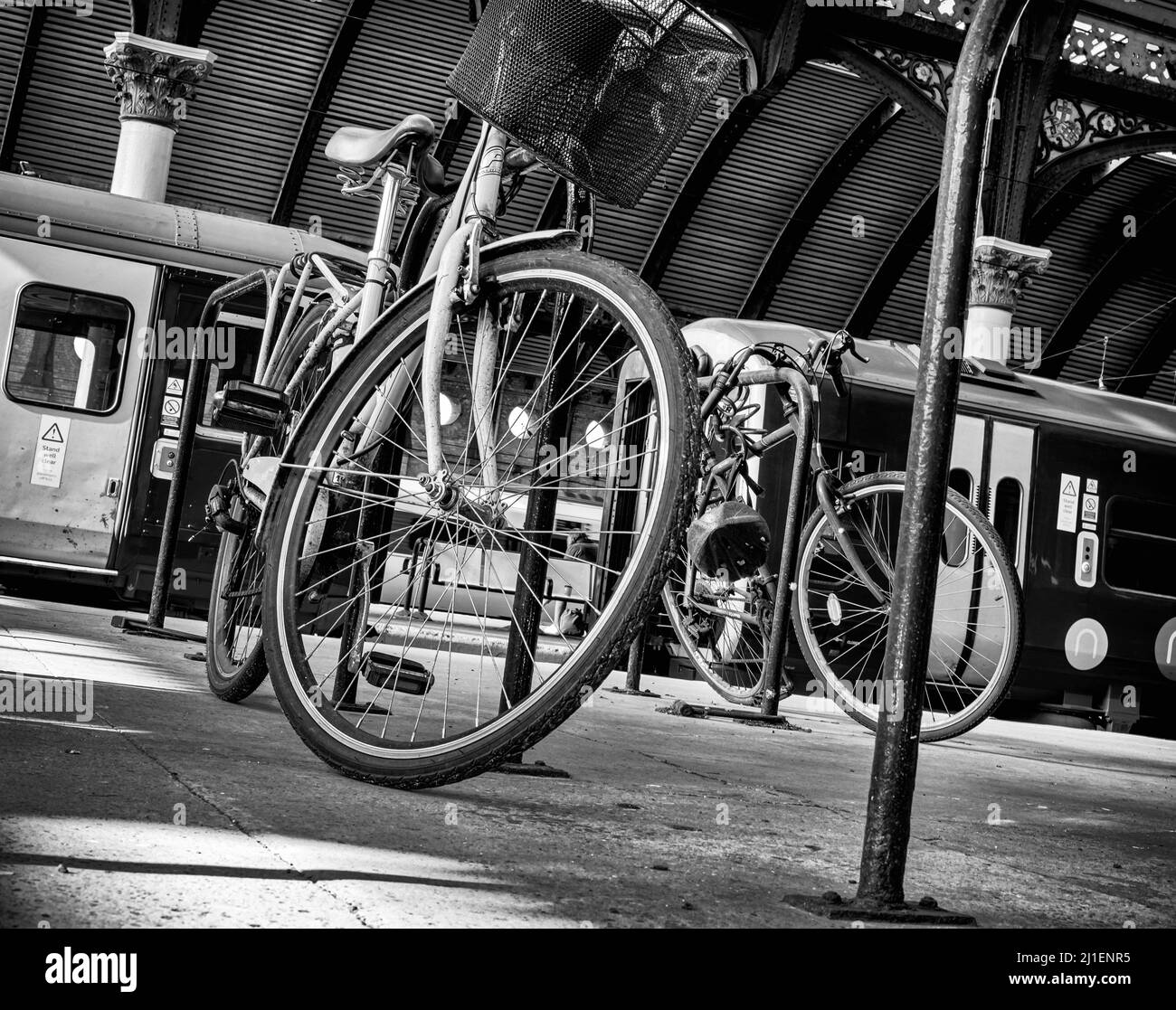 Piattaforma della stazione ferroviaria con una bicicletta in primo piano. Due treni sono dietro e una tettoia ricurva ornata del 19th secolo è in testa. Foto Stock