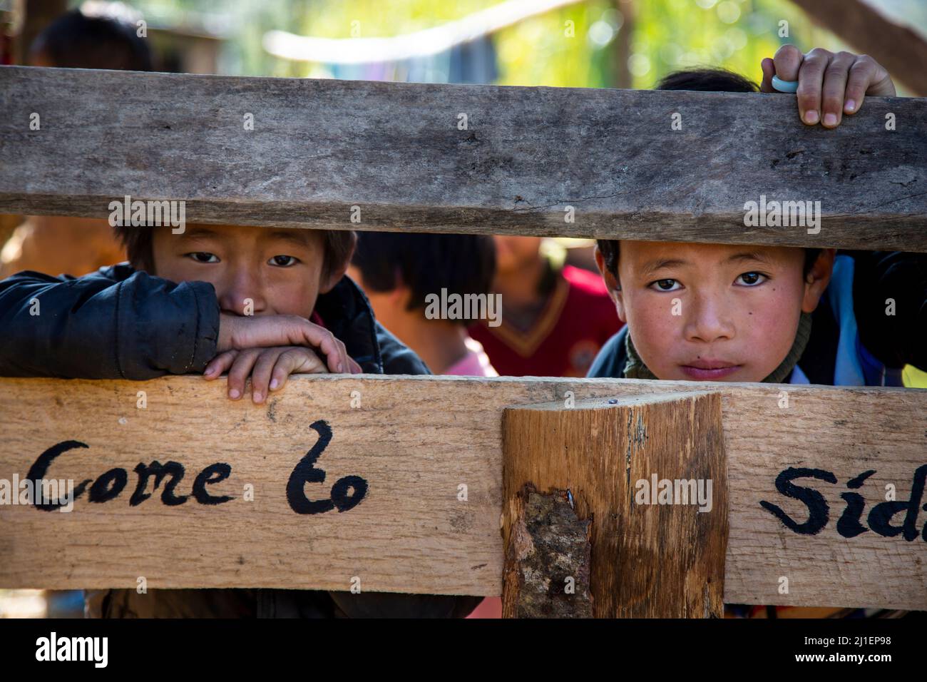 Vista di due simpatici bambini che guardano nella fotocamera dal gap tra due tavole di legno. Foto Stock