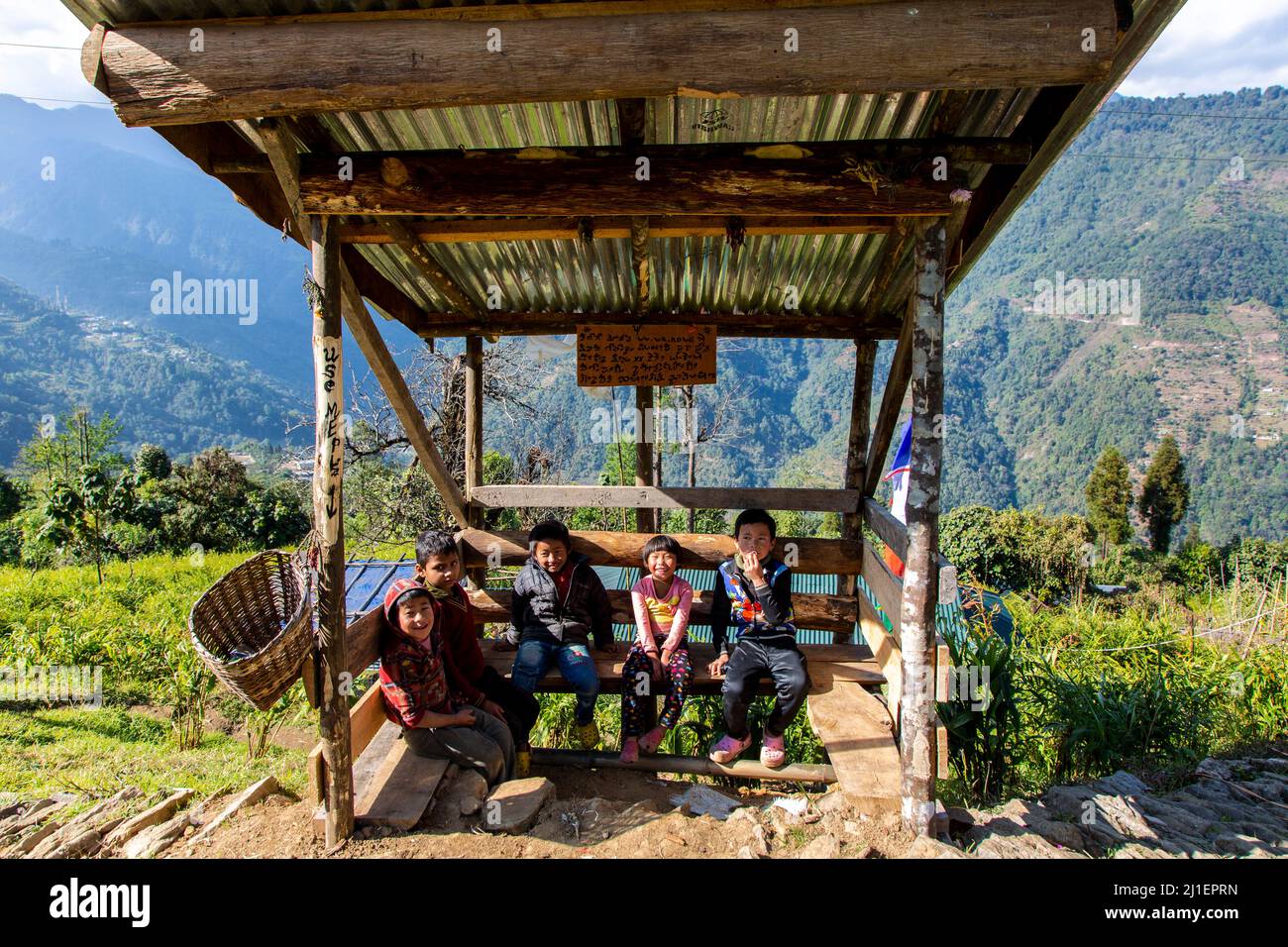 Vista di un gruppo di bambini locali seduti in un rifugio per autobus in un villaggio a Pelling Foto Stock