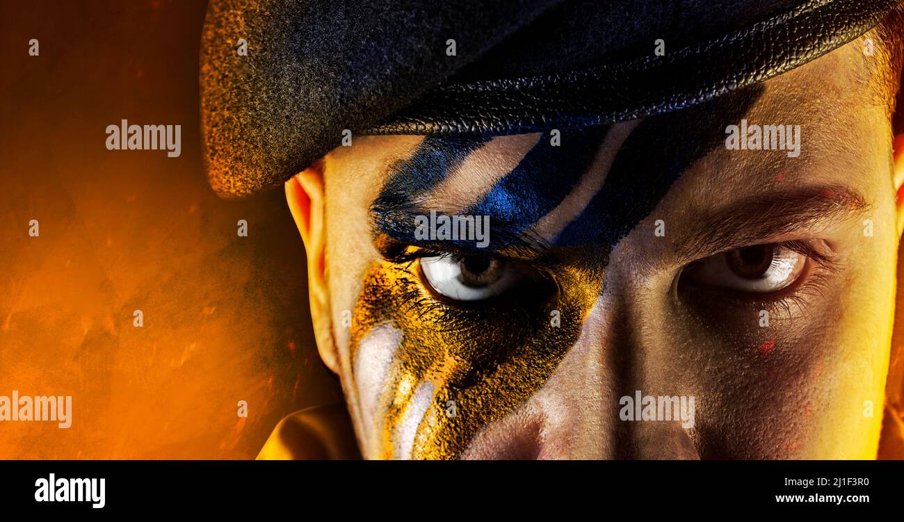 Foto del soldato militare ucraino dipinto faccia in beretta nera uniforme su sfondo bruciato. Foto Stock
