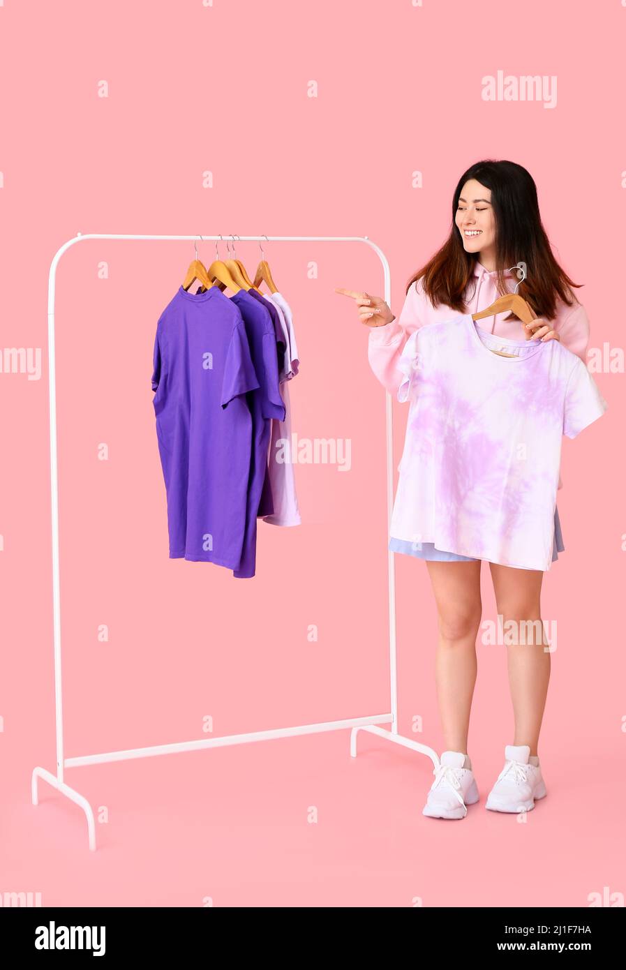 Giovane donna asiatica con t-shirt e rack su sfondo rosa Foto Stock