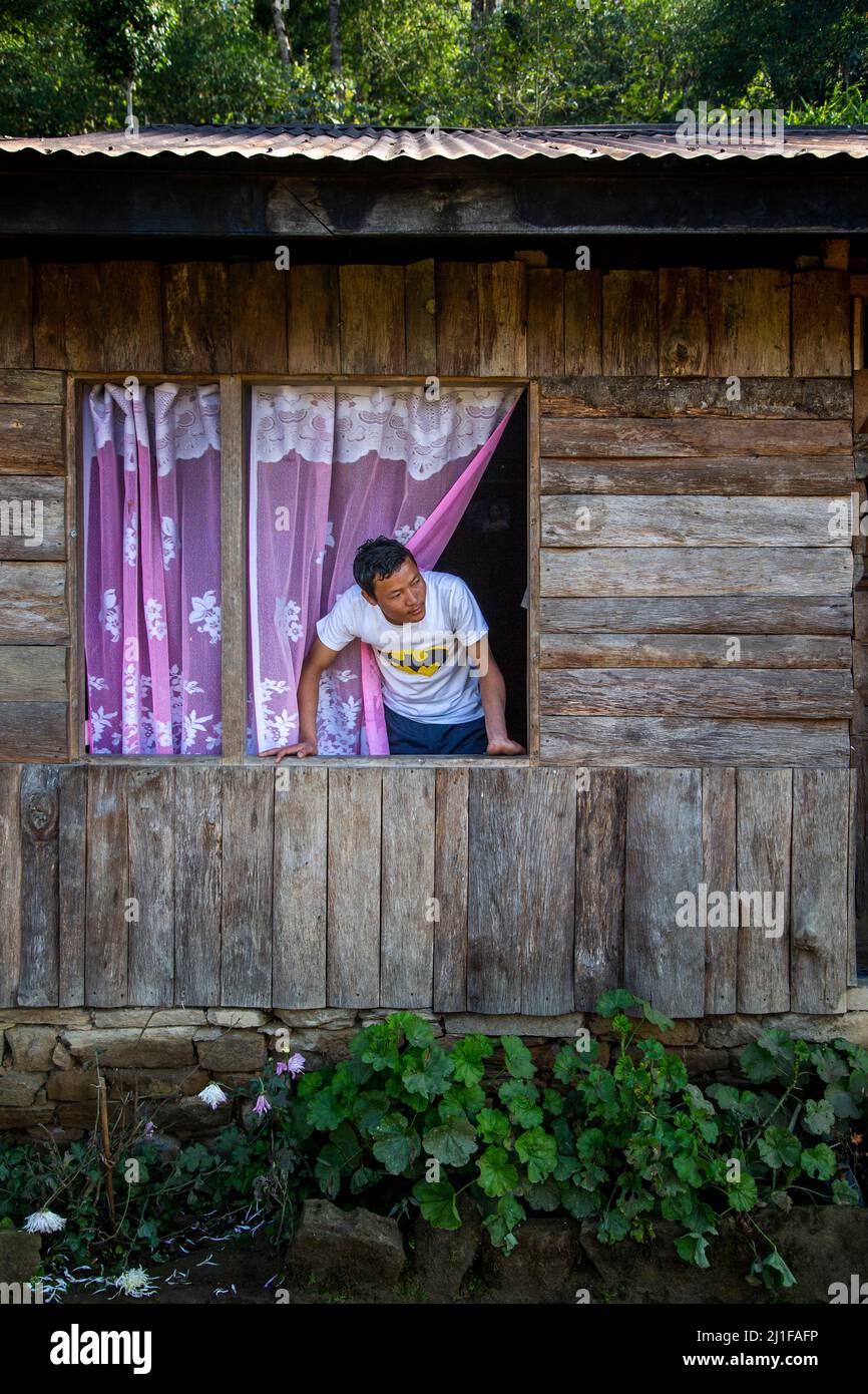 Vista di un ragazzo di villaggio che guarda fuori dalla finestra della sua capanna di legno Foto Stock