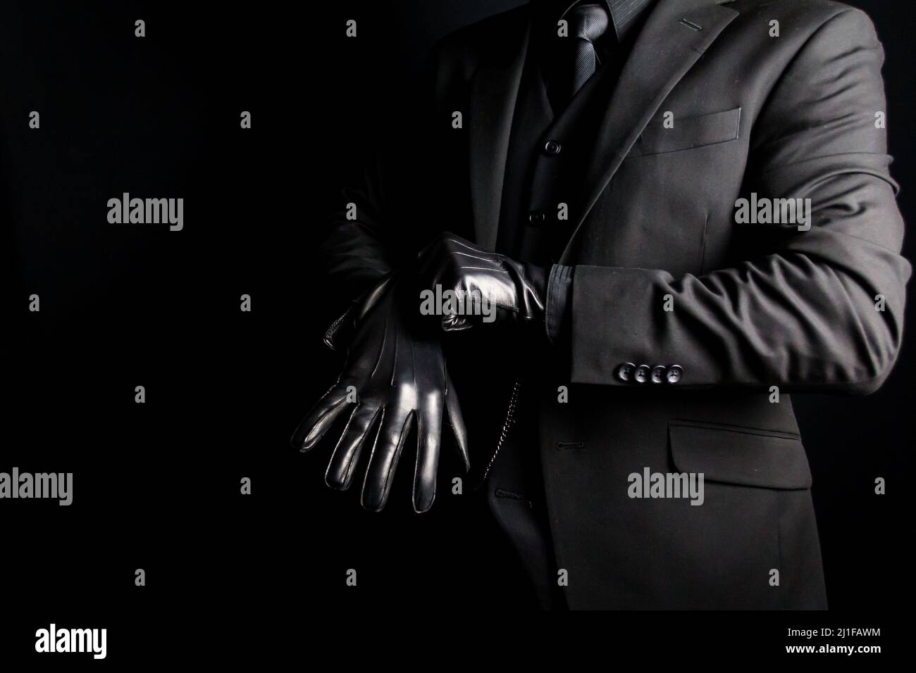 Portrait of Man in Dark Suit tirando i guanti in pelle su sfondo nero. Concetto di Gangster o Mafia Hit Man. Foto Stock