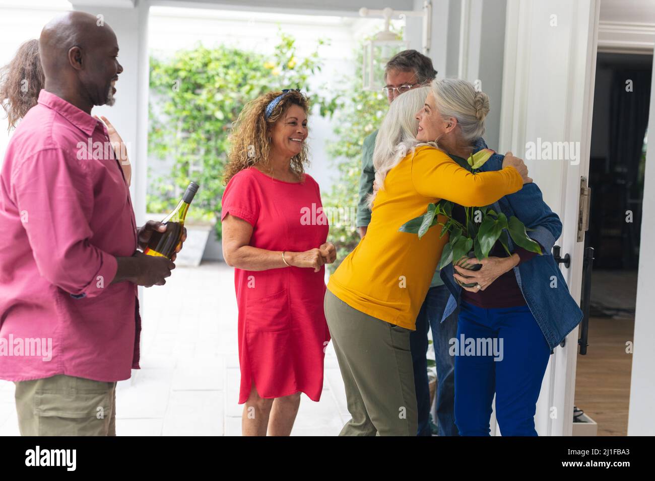 Donna anziana che accoglie gli amici multirazziali all'ingresso durante la festa della casa Foto Stock