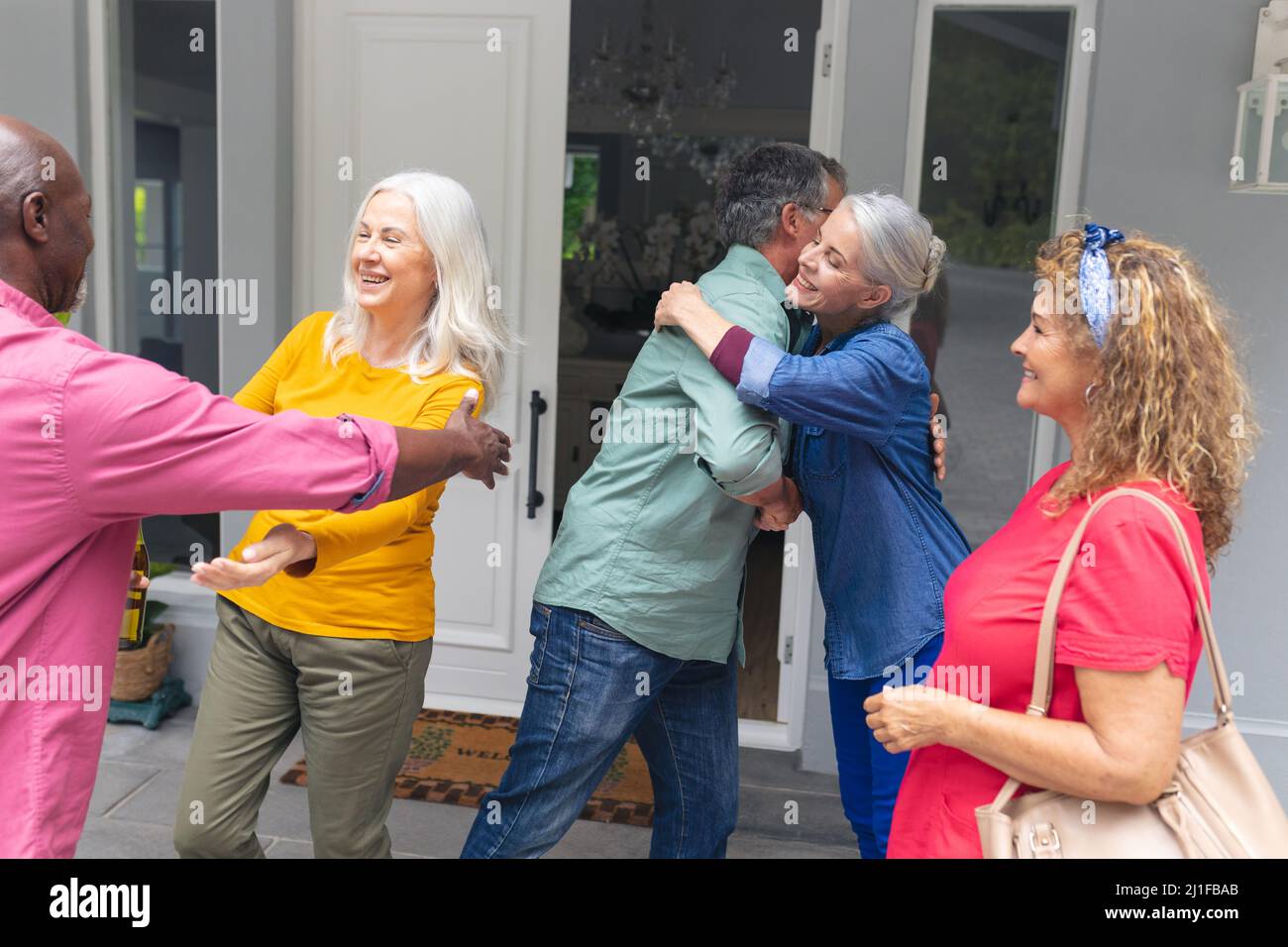 Amici multirazziali anziani felici si salutano a vicenda all'ingresso durante la festa della casa Foto Stock