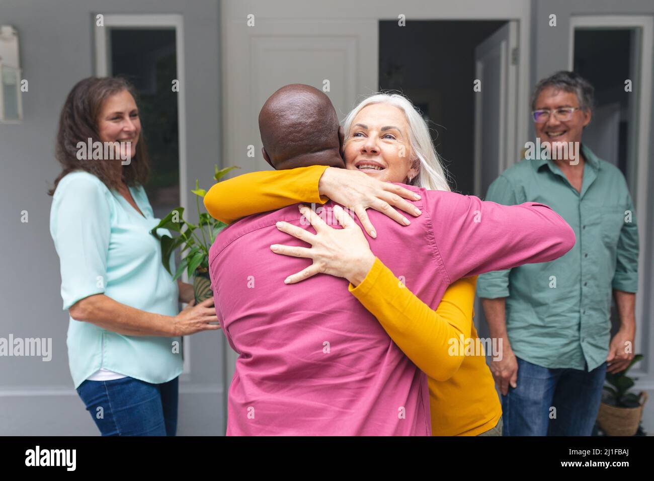 Amici anziani multirazziali maschili e femminili che si abbracciano all'ingresso durante la festa della casa Foto Stock