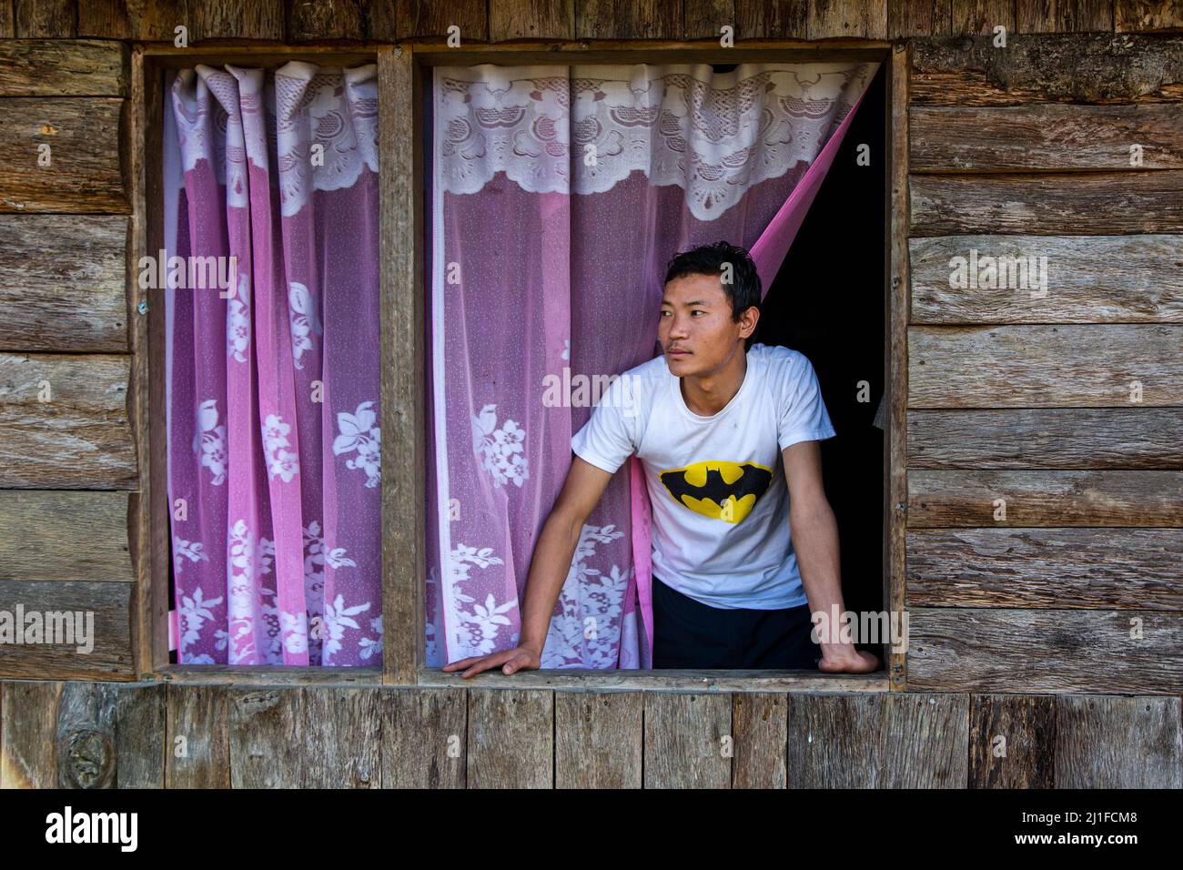 Vista di un ragazzo di villaggio che guarda fuori dalla finestra della sua capanna di legno Foto Stock
