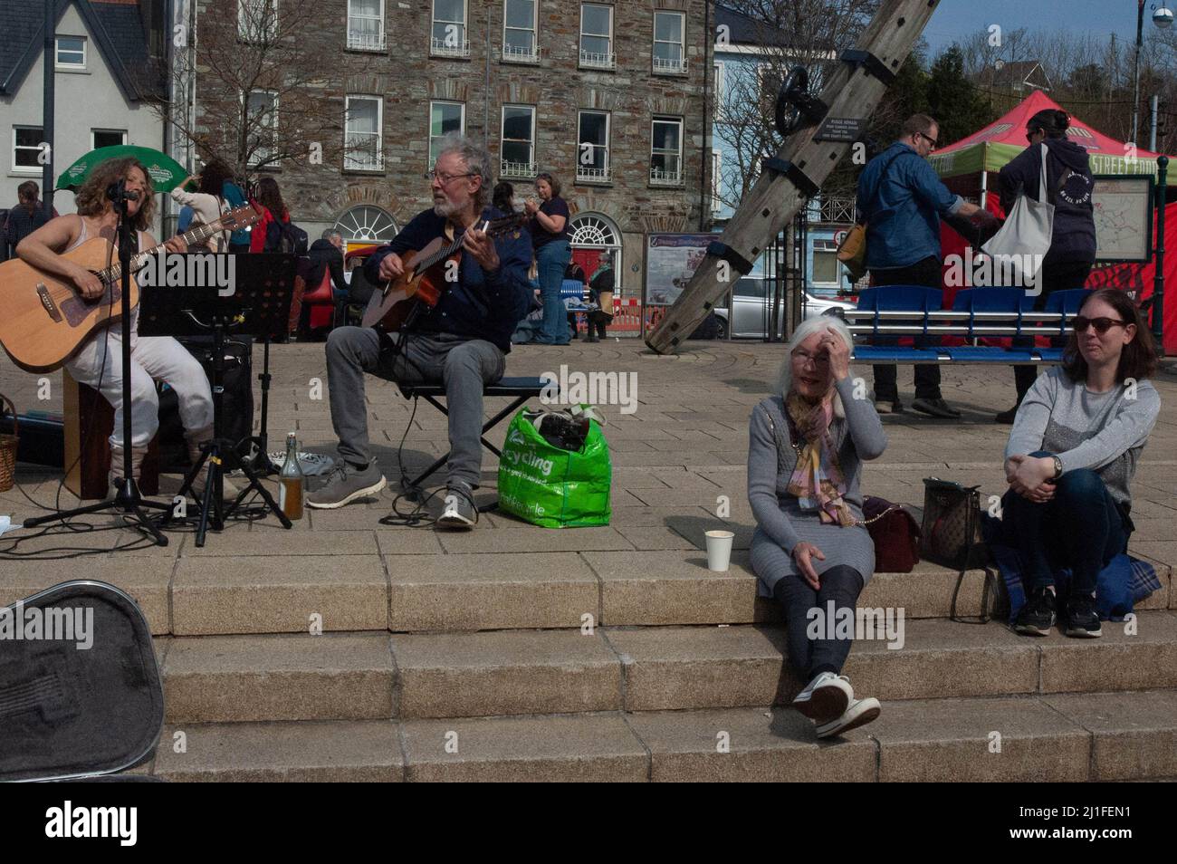 Bantry, West Cork, Irlanda, venerdì 25 marzo 2022; il sole brilla sul mercato di Bantry oggi attirando la gente fuori. Molta gente dove fuori in t-shirt con tempratures che colpiscono 22 gradi. Persone che godono di una serenata musicale al mercato settimanale. Credit ed/Alamy Live News Foto Stock