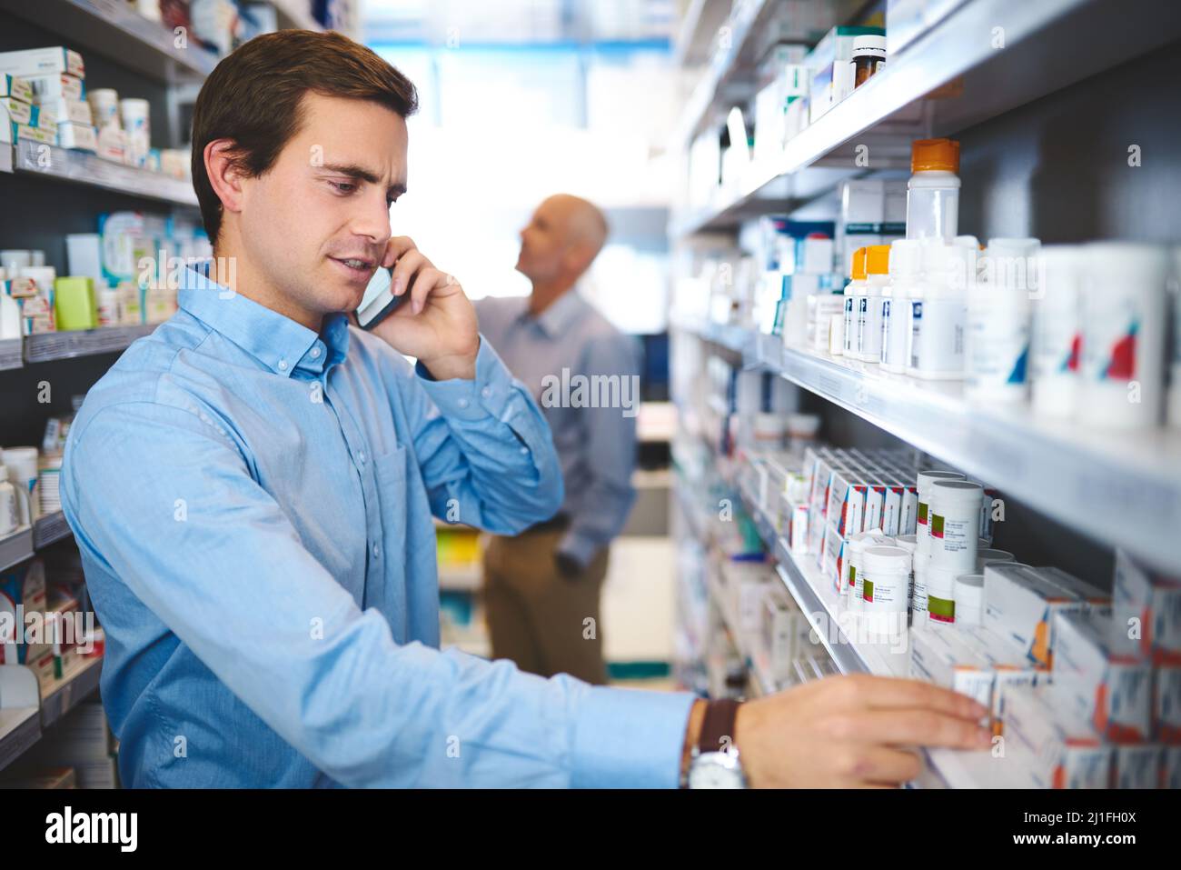 Che cosa è di nuovo il nome. Scatto corto di un bel giovane uomo che fa una phonecall mentre cerca il farmaco in una farmacia. Foto Stock