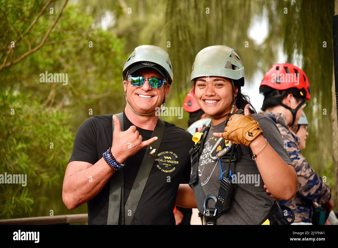 La guida del tour e i partecipanti alla zipline sorridono e danno un gesto a mano shaka in una piattaforma di legno alle Arrampicata Keana Farms, North Shore, Kahuku, HI, USA Foto Stock