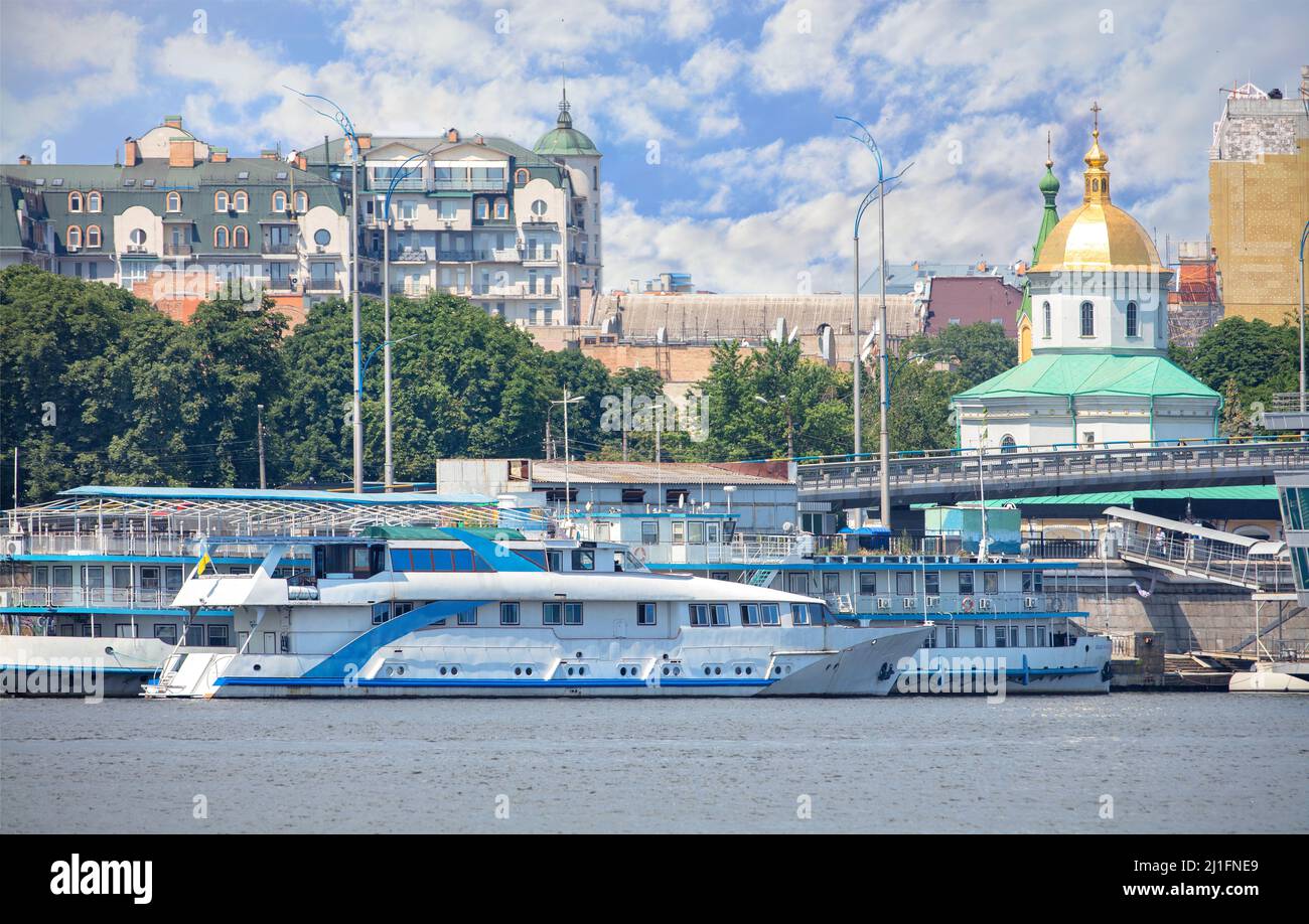 Barca da piacere tram fluviali al molo sul lungofiume del Dnipro sullo sfondo dell'architettura urbana di Kyiv e il cielo nuvoloso blu. Foto Stock