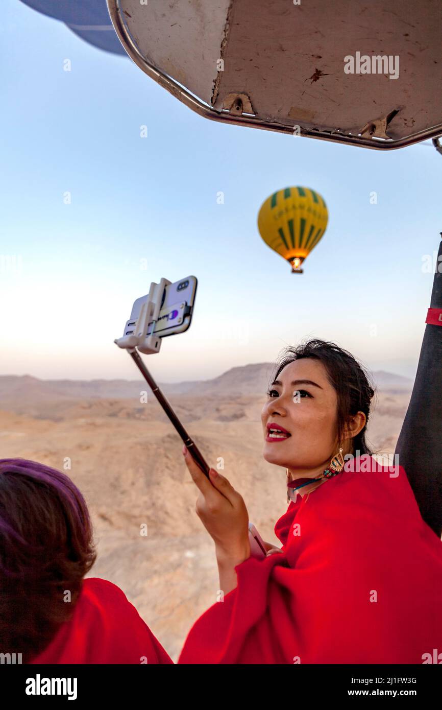 Bella giovane donna in rosso che prende selfie mentre vola in una mongolfiera a Luxor Foto Stock