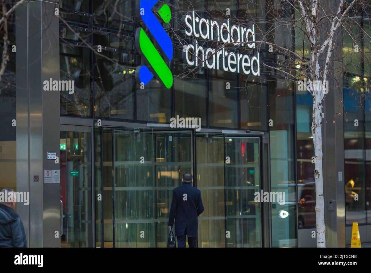 Un pedone passa davanti alle persone che entrano in Standard Chartered nella Città di Londra la mattina, come lavoro-da-casa guida è stato rimosso la settimana scorsa a en Foto Stock