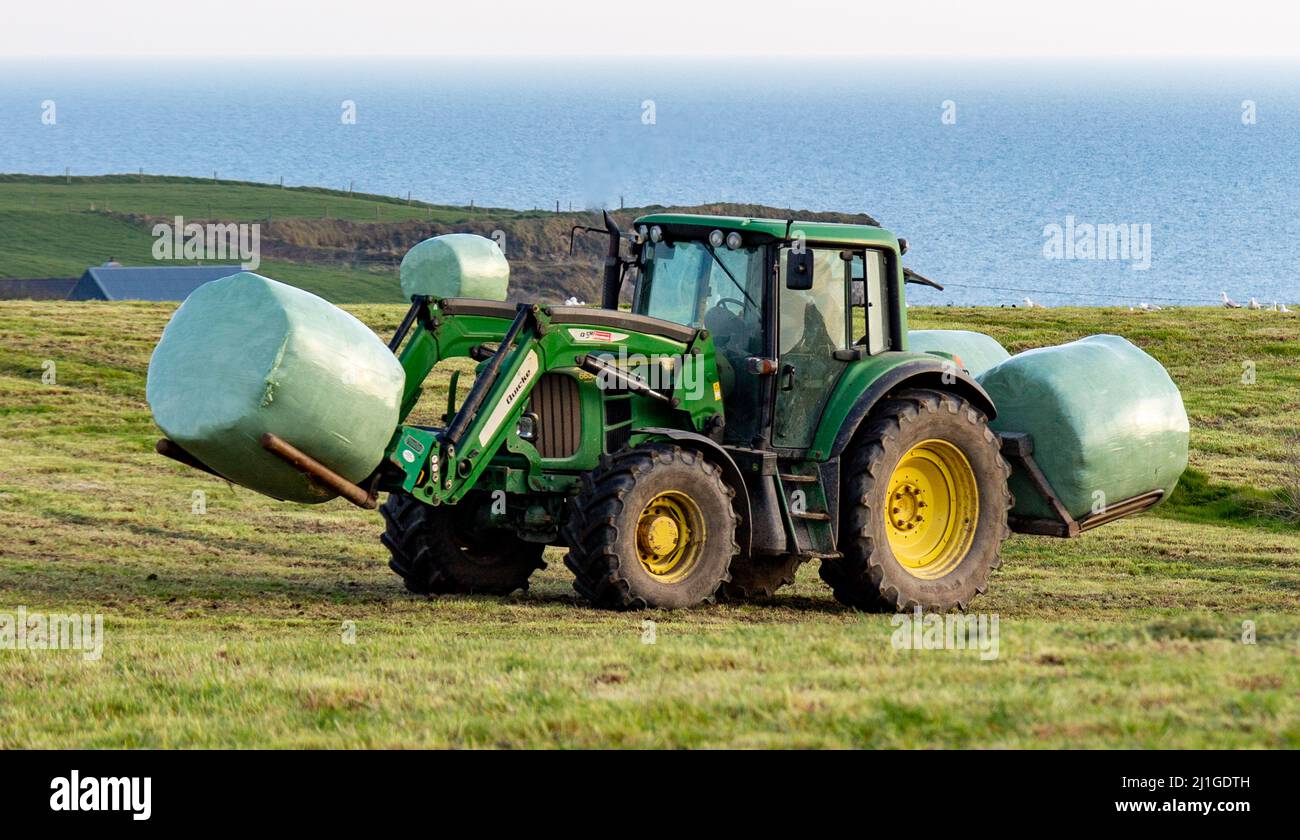 Trattore che carica balle di insilato sul rimorchio nella campagna irlandese Foto Stock