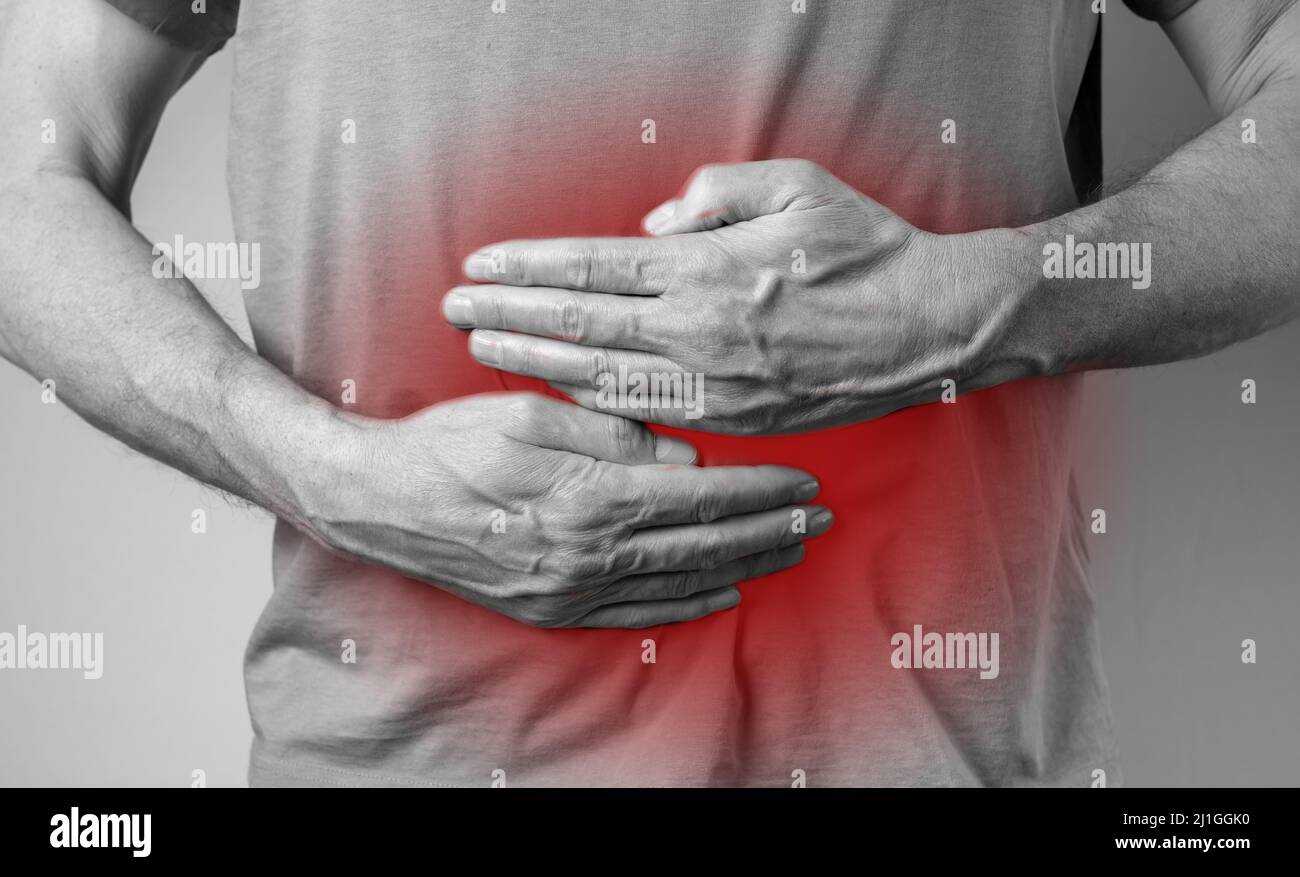 Uomo che soffre di mal di stomaco e che tiene le mani sullo stomaco con punto rosso primo piano. Concetto di salute e medicina. Indigestione, infiammazione. Foto di alta qualità Foto Stock