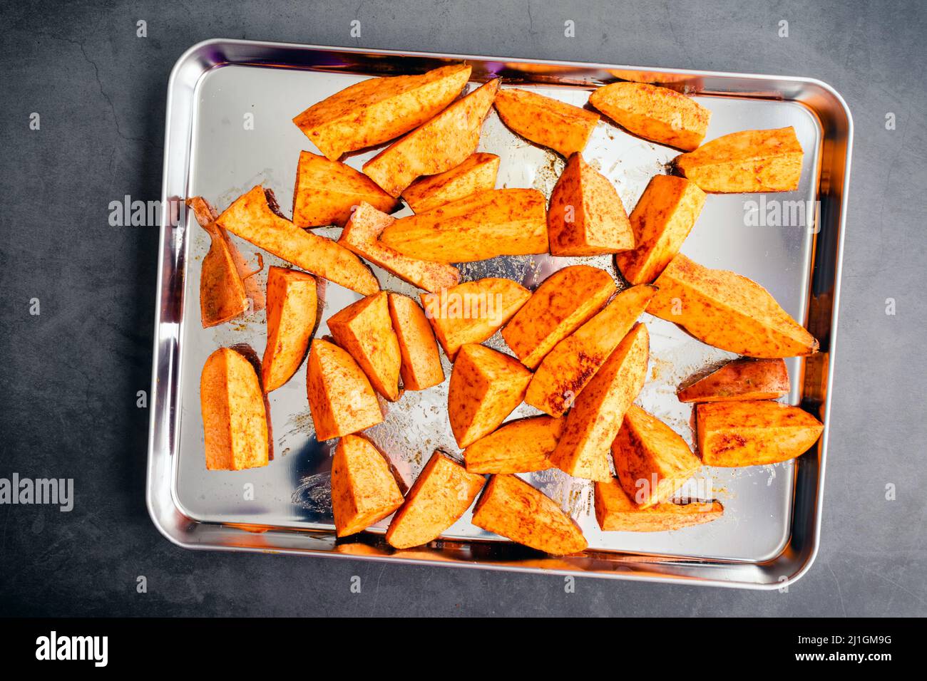 Spicchi di patate dolci crude su una teglie: Spicchi di patate dolci non cotte conditi con olio d'oliva, cumino e paprika affumicata Foto Stock