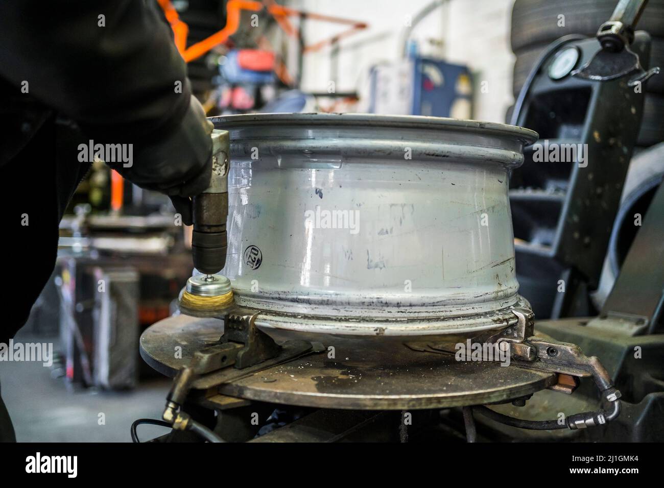 Officina del garage per pneumatici. Il personale del garage pulisce il cerchione interno di una ruota in lega con una spazzola metallica elettrica prima del montaggio degli pneumatici. Foto Stock