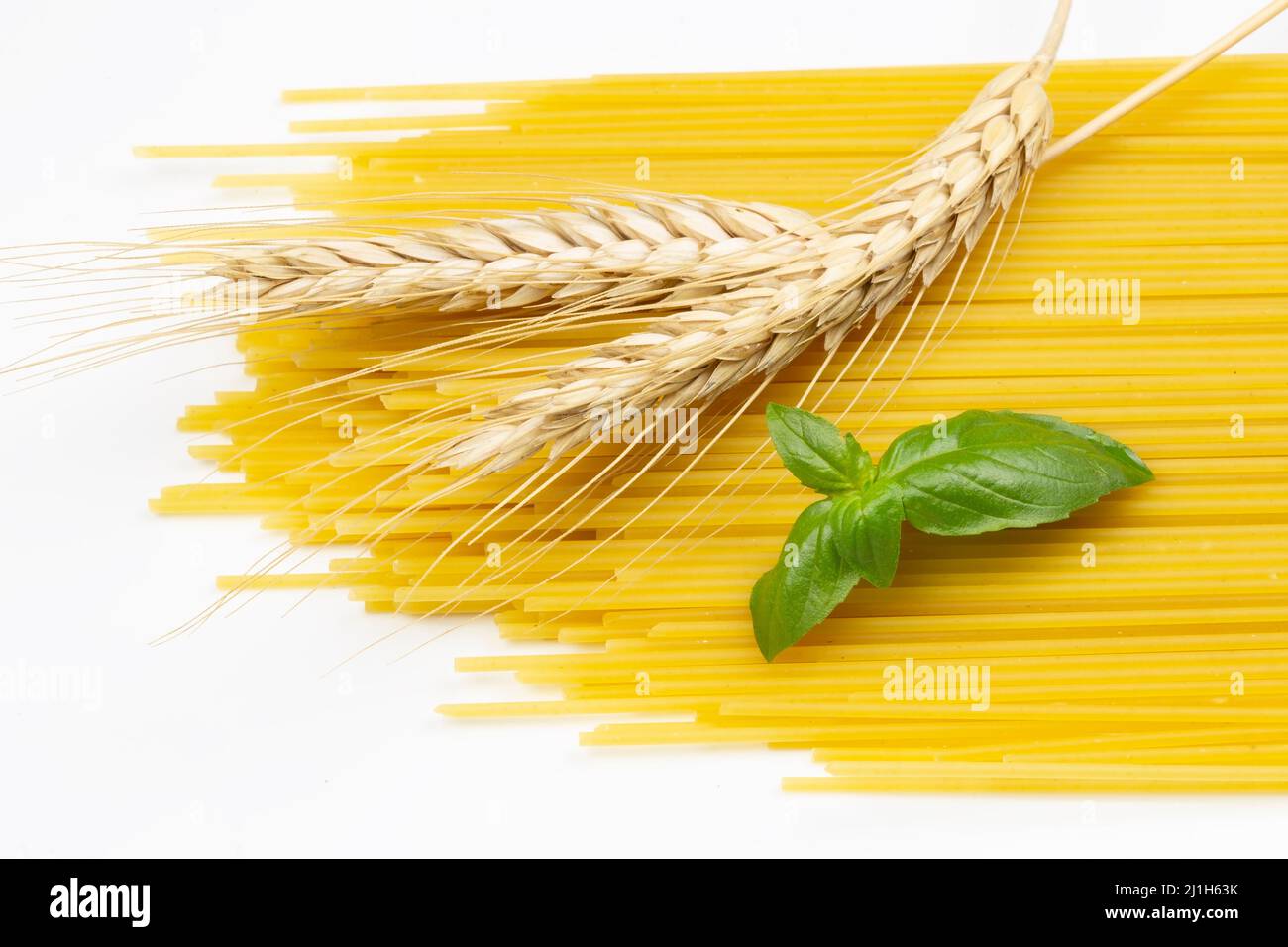 Spaghetti con le spighe di grano e basilico su sfondo bianco Foto Stock