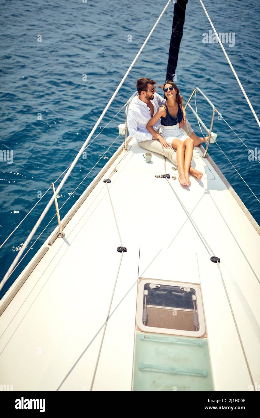 Una giovane coppia innamorata è seduta in un abbraccio sulla prua dello yacht e avere un buon tempo mentre si viaggia in una bella giornata di sole sul mare. Estate, mare, Foto Stock