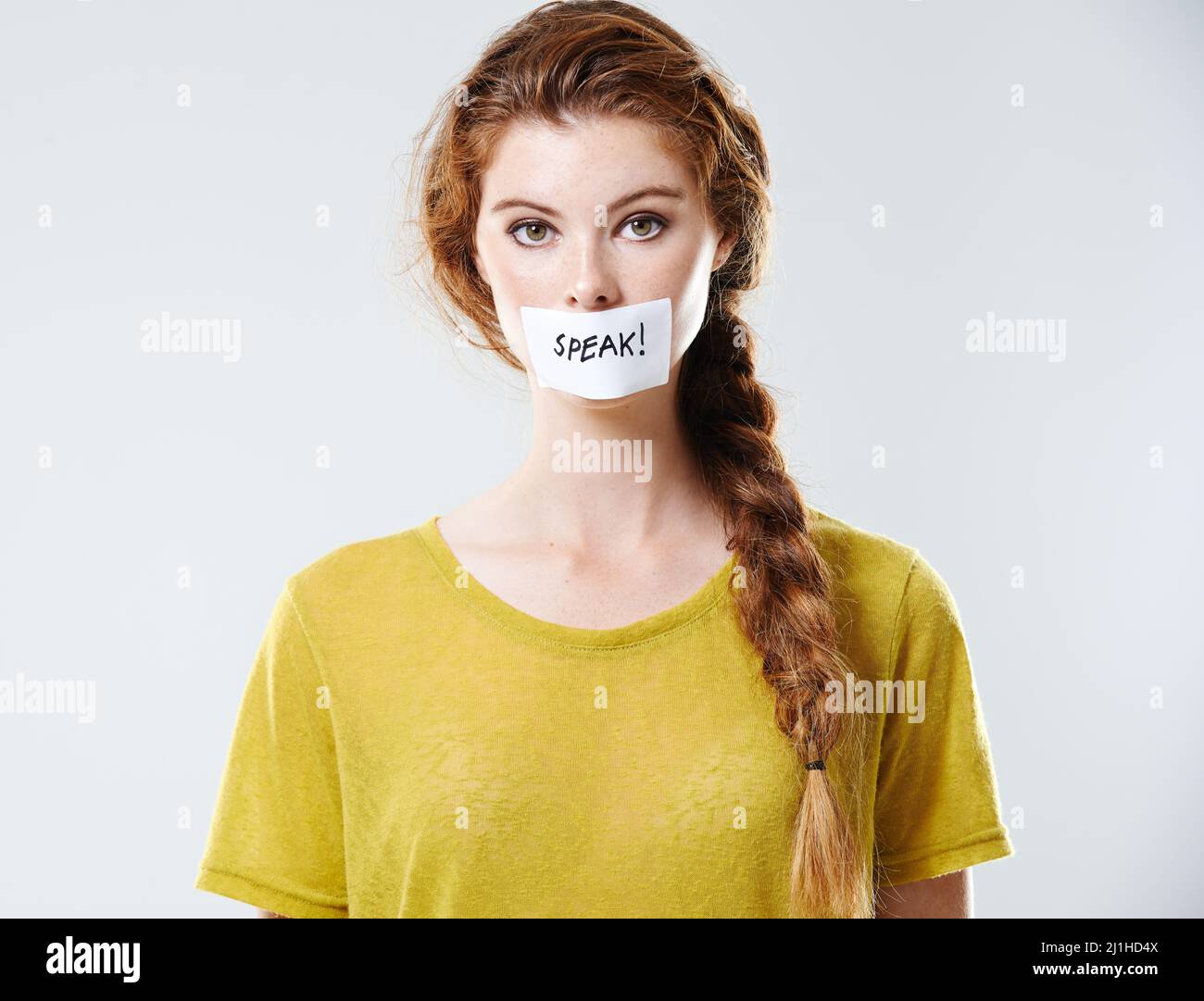 USA la tua voce. Ritratto corto studio di una giovane donna con un'etichetta che dice parlare coprendo la sua bocca. Foto Stock