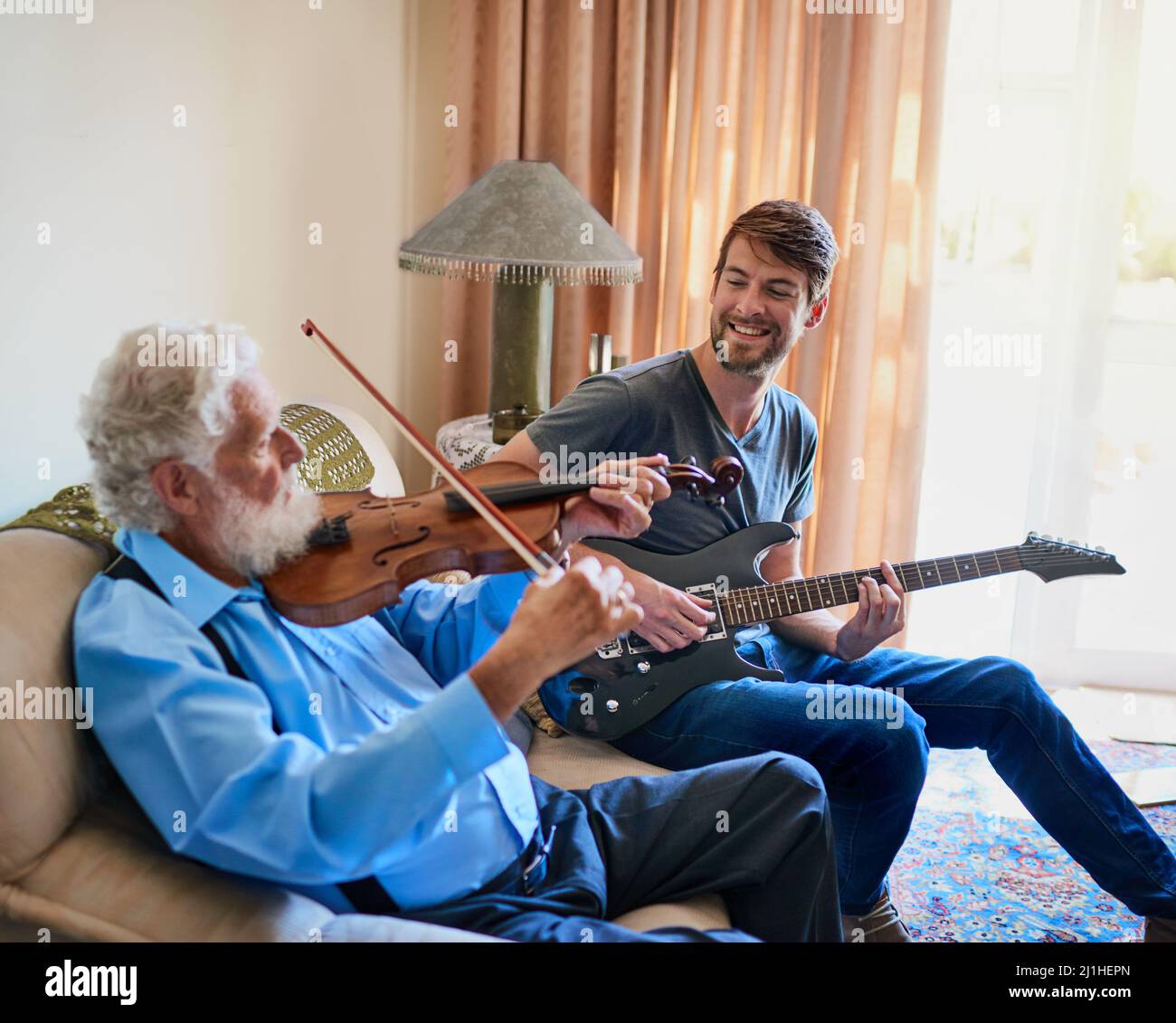 Legarsi attraverso la loro musica. Scatto di un giovane che suona la chitarra elettrica mentre il nonno anziano suona il violino sul divano. Foto Stock