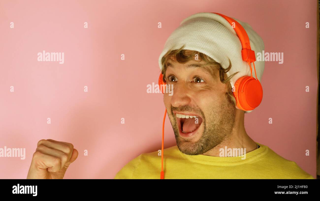Giovane uomo indossare cuffie giallo camicia ascoltare musica cantare voce record isolato su semplice pastello rosa sfondo ritratto studio. Foto Stock