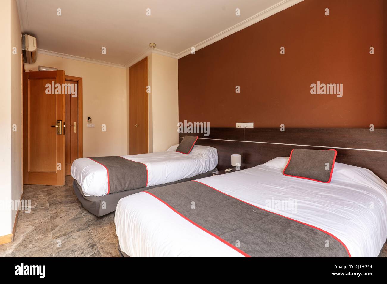 Camera d'hotel con letti gemelli con testiera in legno e cuscini marroni con finiture rosse e pavimenti in marmo scuro Foto Stock