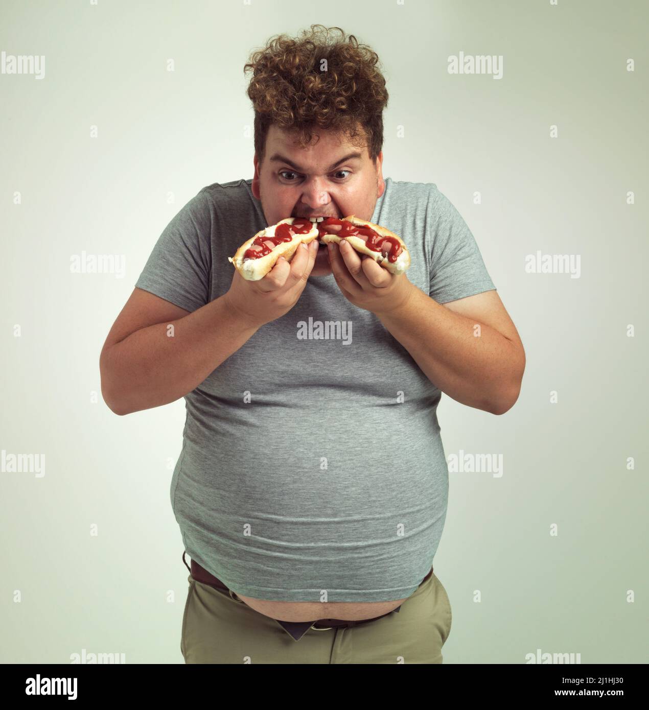 Non riesco ad avere abbastanza di questi hotdog. Studio girato di un uomo in sovrappeso che mangia due hotdog alla volta. Foto Stock