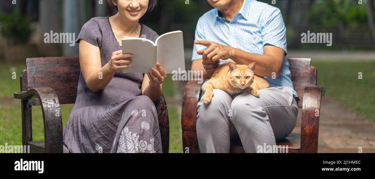 Coppia e gatto di mezza età sono relax seduti su panca in cortile. Foto Stock