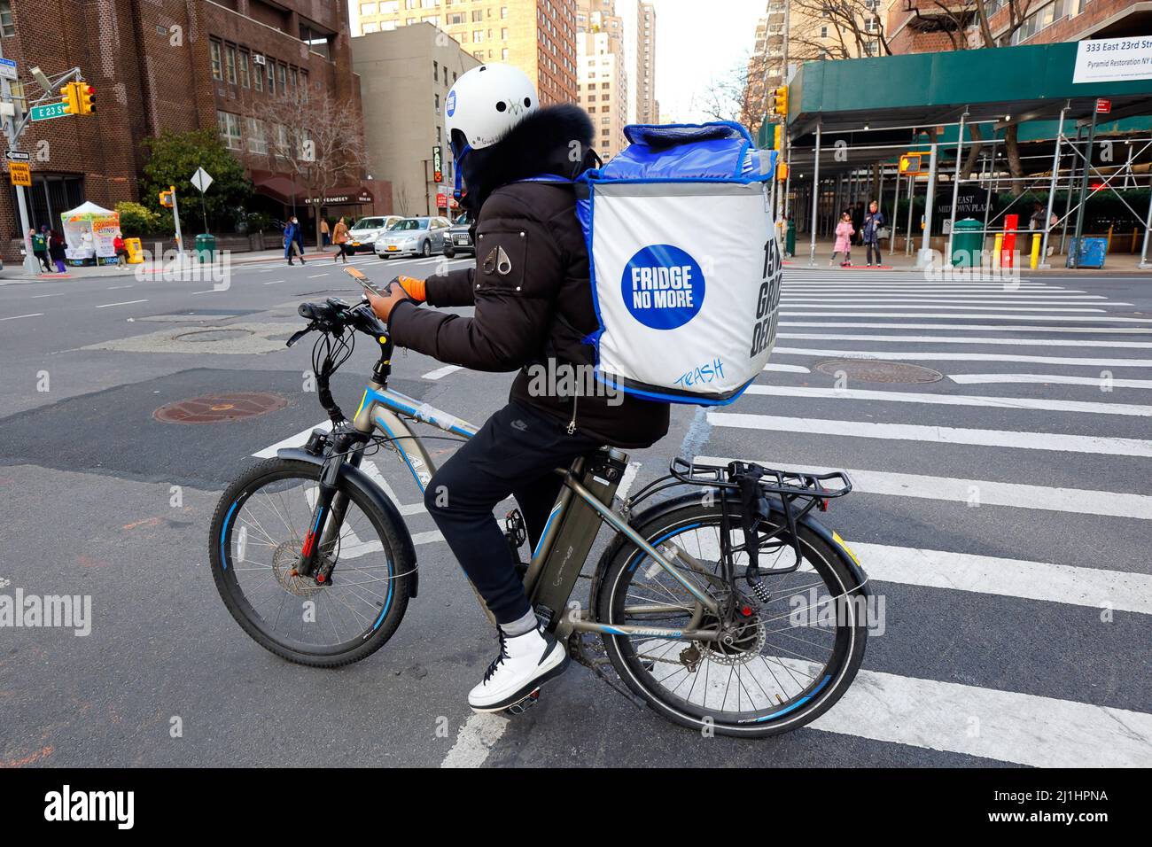 Un Frigo non ci sono più persone che si consegnano su una bicicletta elettrica, tiene uno smartphone con indicazioni stradali mentre si fa una pausa a un incrocio di New York City, 3 marzo 2022. Foto Stock Un Frigo non ci sono più persone che si consegnano su una bicicletta elettrica, tiene uno smartphone con indicazioni stradali mentre si fa una pausa a un incrocio di New York City, 3 marzo 2022. Foto Stock