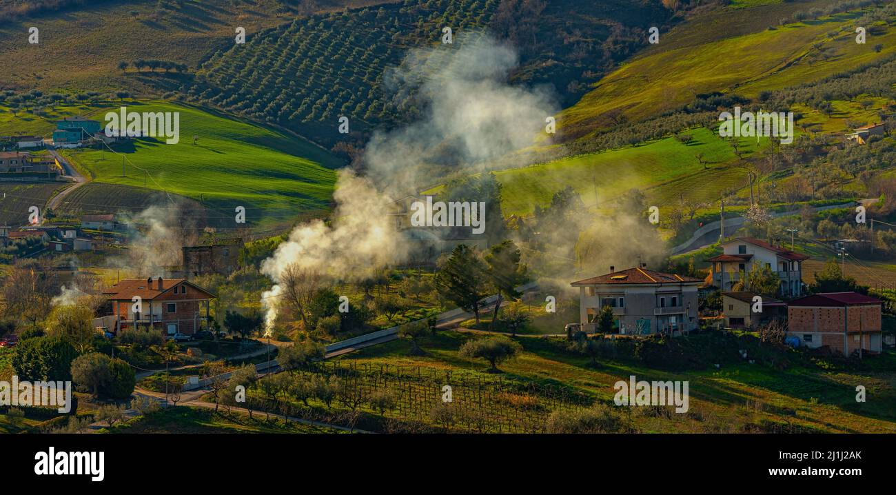 Colonne di fumo da piccoli incendi illuminati da agricoltori per bruciare i resti di potatura primaverile. Abruzzo, Italia, Europa Foto Stock