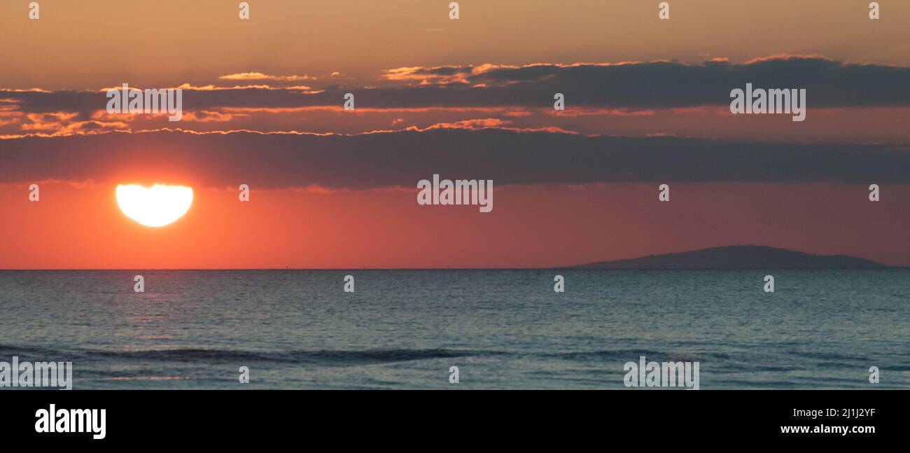 Paesaggio di un tramonto con il sole che scende dietro le nuvole sopra il mare in un'atmosfera rossa Foto Stock