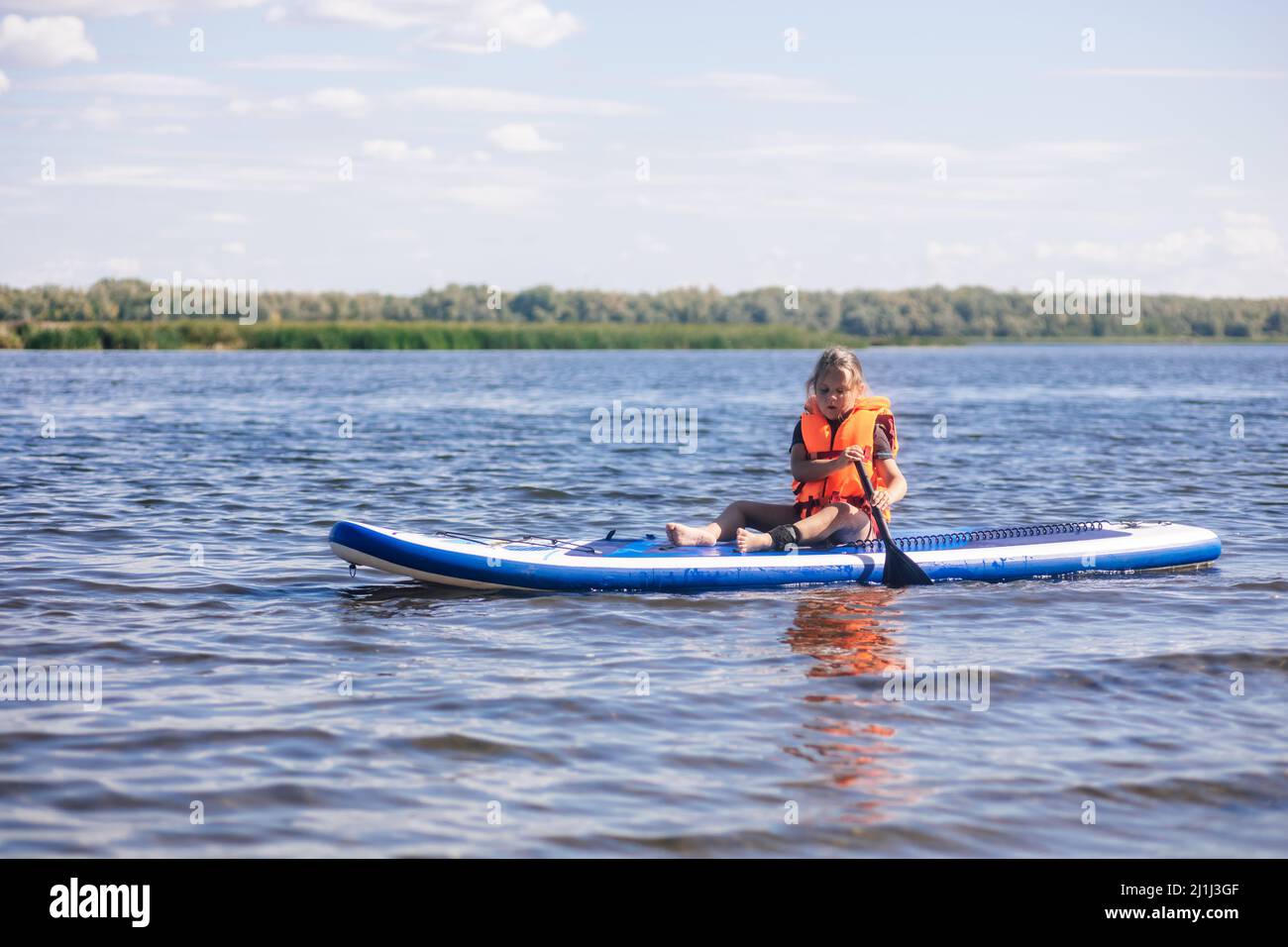 Femmina bambino sup imbarco sul suo proprio lago calmo con il remo in mani guardando ondulazione acqua in giubbotto vita giubbotto. Vacanze attive. Inculcatione di amore Foto Stock