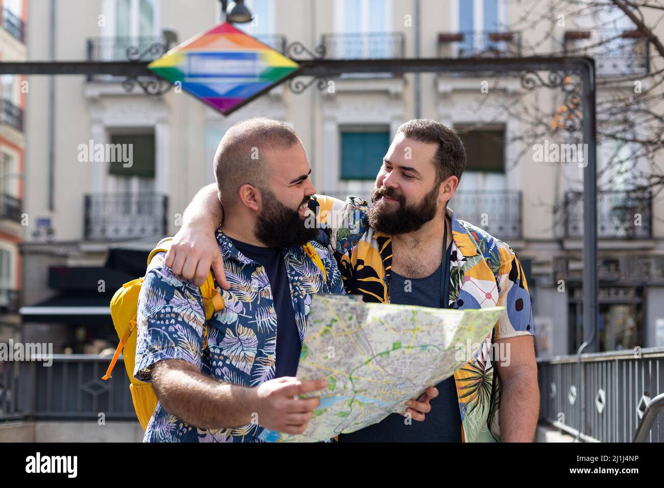 Giovane coppia gay con mappa turistica all'uscita di una stazione dei trasporti. Concetto di persone che viaggiano e vacanze. Foto Stock